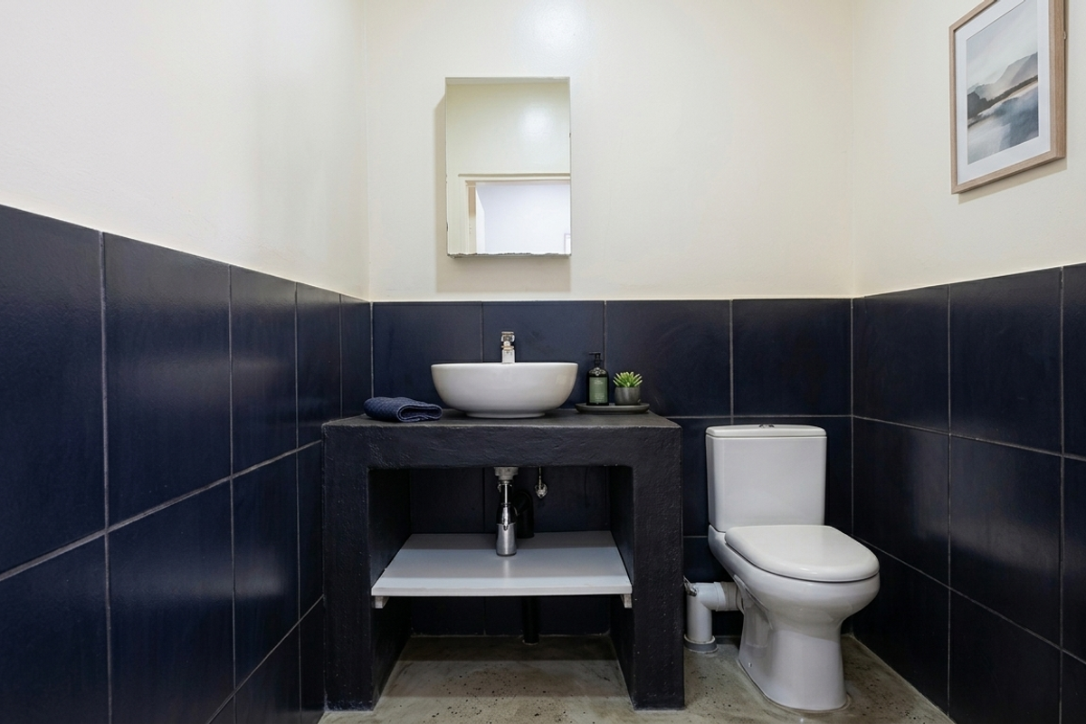 A modern bathroom featuring a dark tiled half-wall, a concrete vanity with a vessel sink, and a standard toilet.