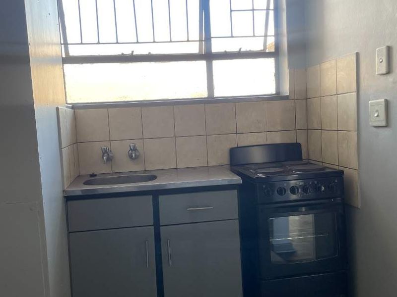 A compact kitchen area featuring a stainless steel sink, tiled backsplash, and a freestanding stove, offering a functional space ready for modernization.