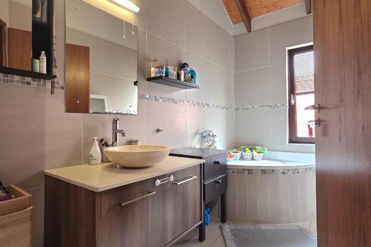 A well-maintained bathroom featuring a modern vanity with a vessel sink, a corner bathtub, tiled walls, and a vaulted timber-paneled ceiling.
