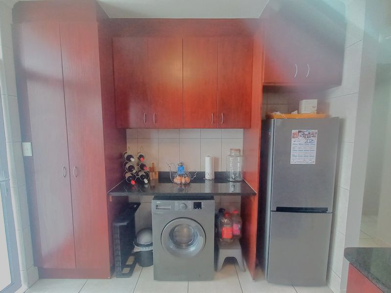 A functional laundry area featuring built-in wooden cabinetry, granite countertops, and tiled finishes, providing efficient storage and utility space.