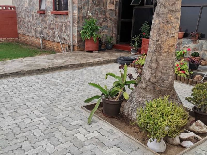 Rear exterior view of the property featuring stone cladding, paved courtyard area, and established garden elements.