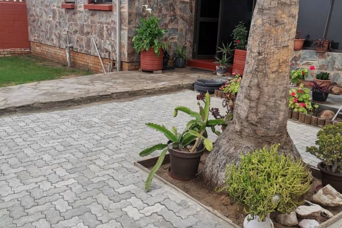 Rear exterior view of the property featuring stone cladding, paved courtyard area, and established garden elements.