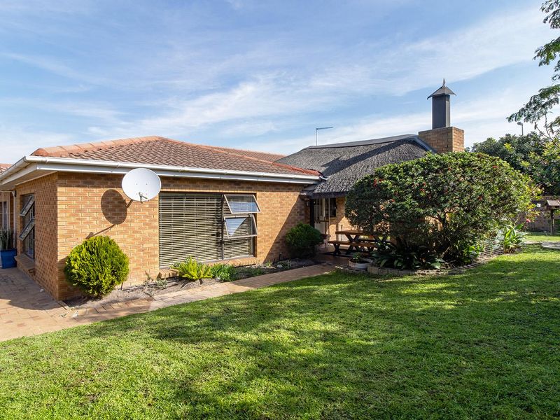 Rear view of the house featuring a combination of brick and thatch roofing, a brick chimney, and a paved walkway leading to the garden area.