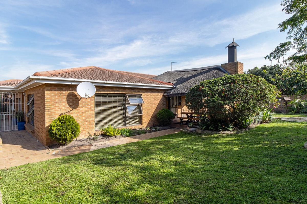 Rear view of the house featuring a combination of brick and thatch roofing, a brick chimney, and a paved walkway leading to the garden area.