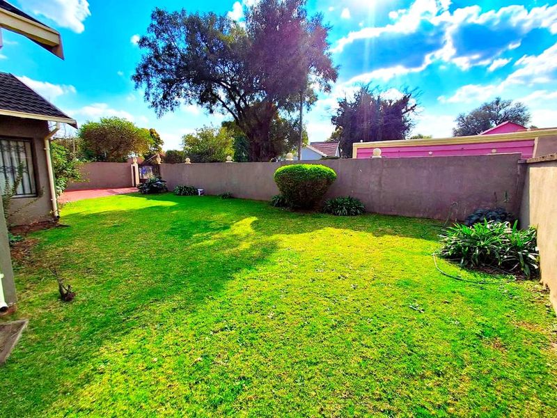 A private rear garden featuring a well-maintained lawn, perimeter boundary wall, and established garden shrubs.