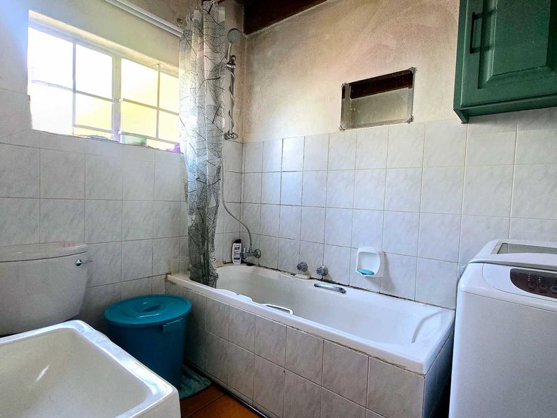 A dated bathroom featuring a bathtub with shower attachment, toilet, and washbasin, requiring renovation to address wall damage and modernize finishes.