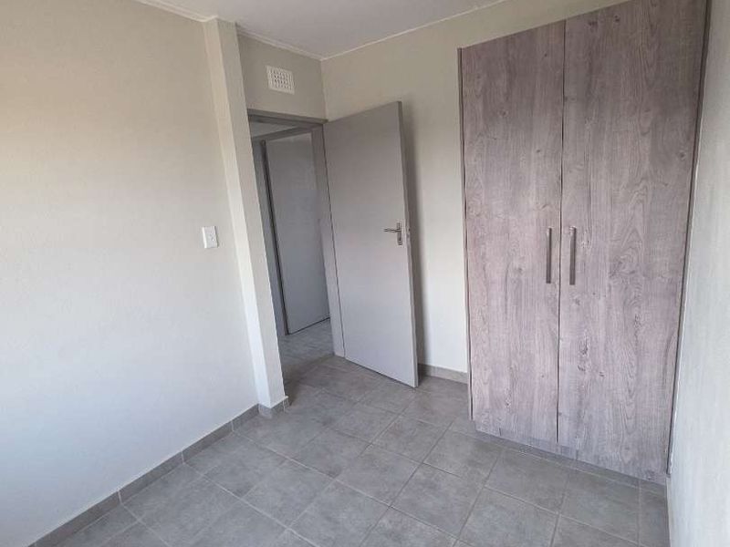 A clean, empty bedroom featuring neutral tiled flooring, a modern wood-finish built-in wardrobe, and a simple ceiling light fixture.