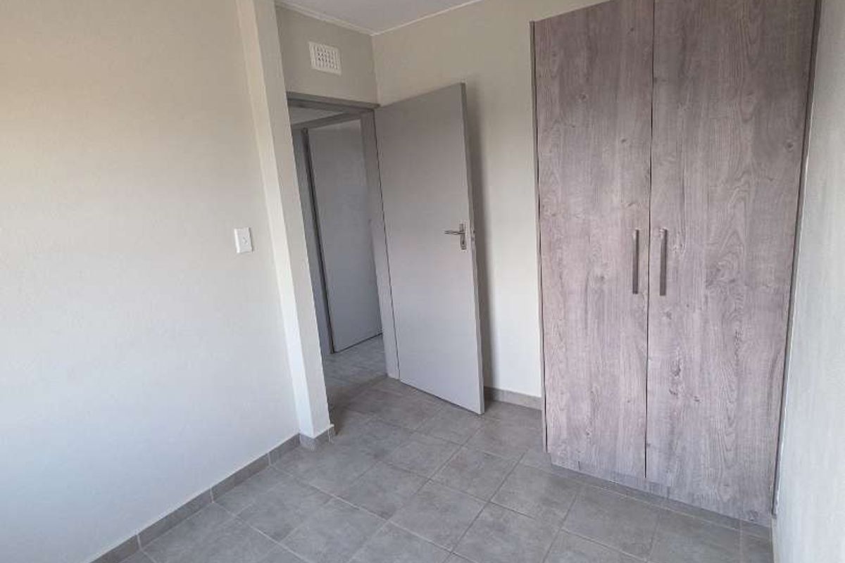 A clean, empty bedroom featuring neutral tiled flooring, a modern wood-finish built-in wardrobe, and a simple ceiling light fixture.