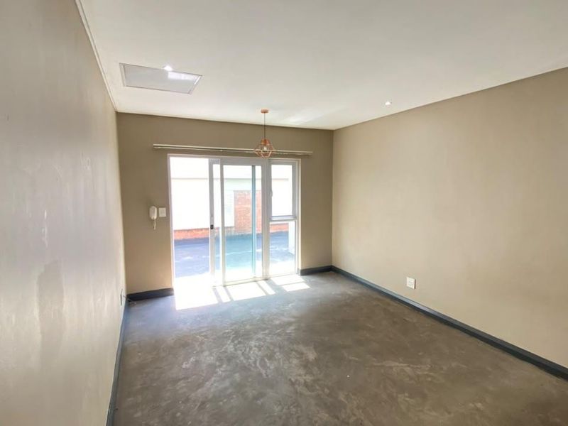 An empty living room featuring neutral walls, recessed lighting, and a sliding glass door providing access to the exterior.