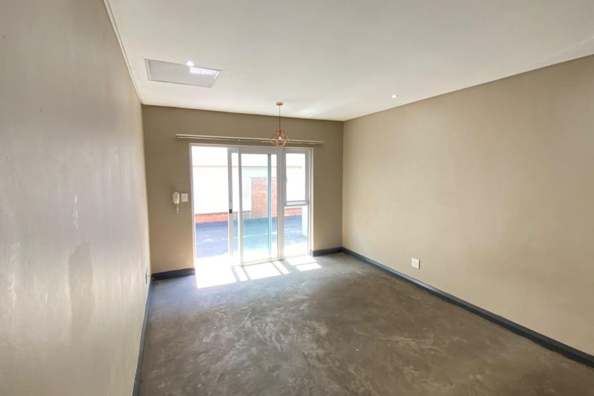 An empty living room featuring neutral walls, recessed lighting, and a sliding glass door providing access to the exterior.