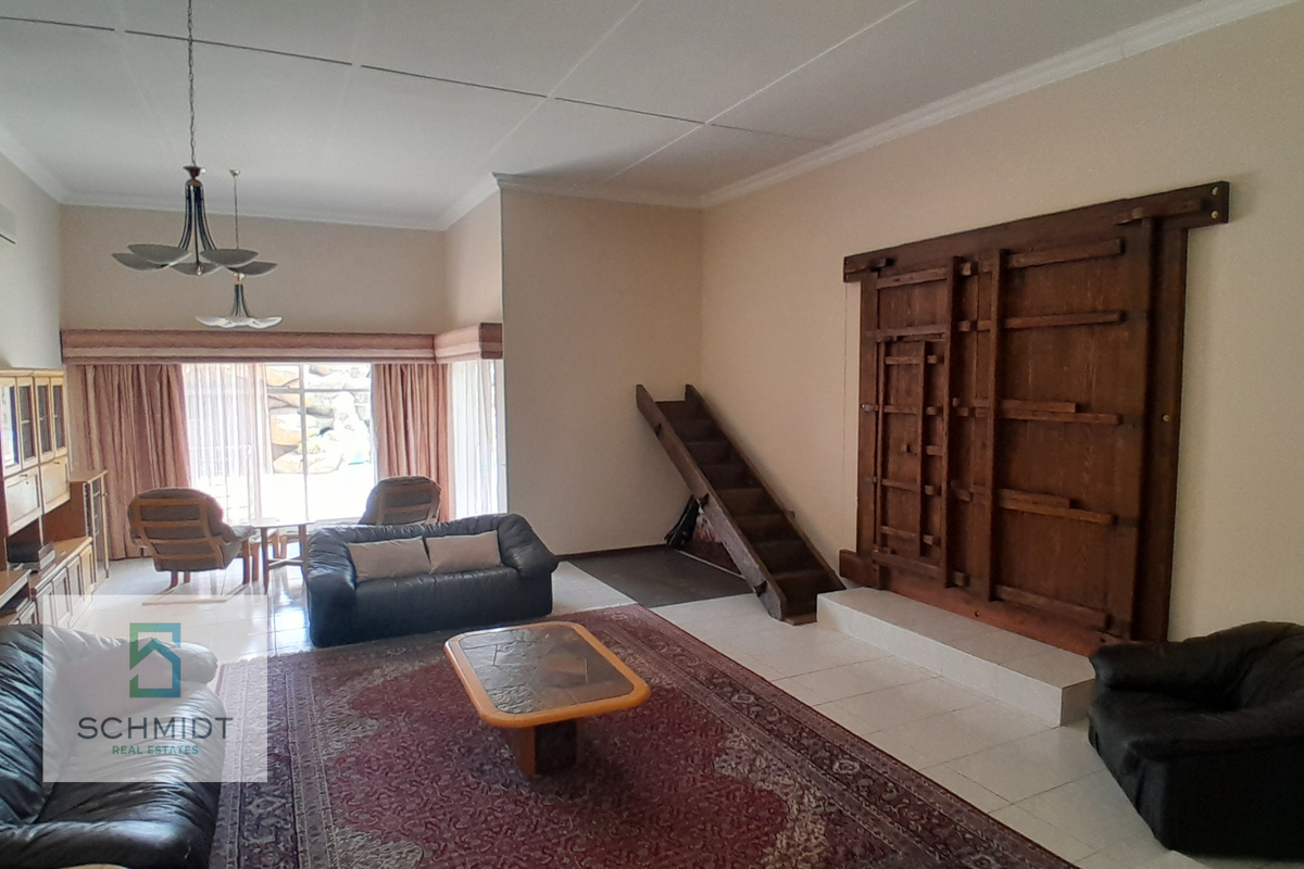 Spacious living room featuring tiled flooring, a unique wooden staircase, decorative wall paneling, and large sliding glass doors leading to the exterior.