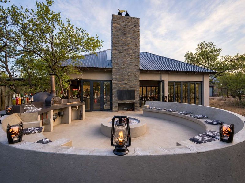 Outdoor entertainment area featuring a stone fireplace, built-in concrete seating, and a fully equipped outdoor kitchen with a pizza oven and sink.