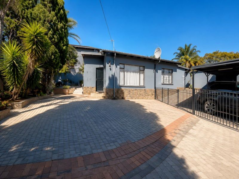 Front exterior view of the house featuring a paved driveway, stone cladding accents, and a covered carport area.