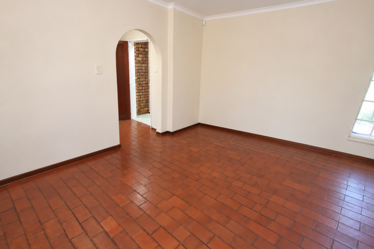 An empty living room featuring traditional terracotta tile flooring, a distinctive arched doorway, and neutral wall finishes.