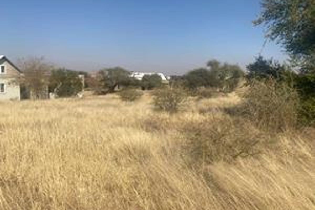 A view of a vacant residential plot featuring dry grass and native vegetation, with neighboring properties visible in the background.
