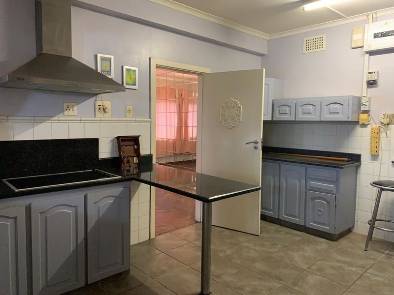 A functional kitchen featuring granite countertops, built-in cabinetry, an electric hob, and an extractor fan, with tiled flooring and splashbacks.