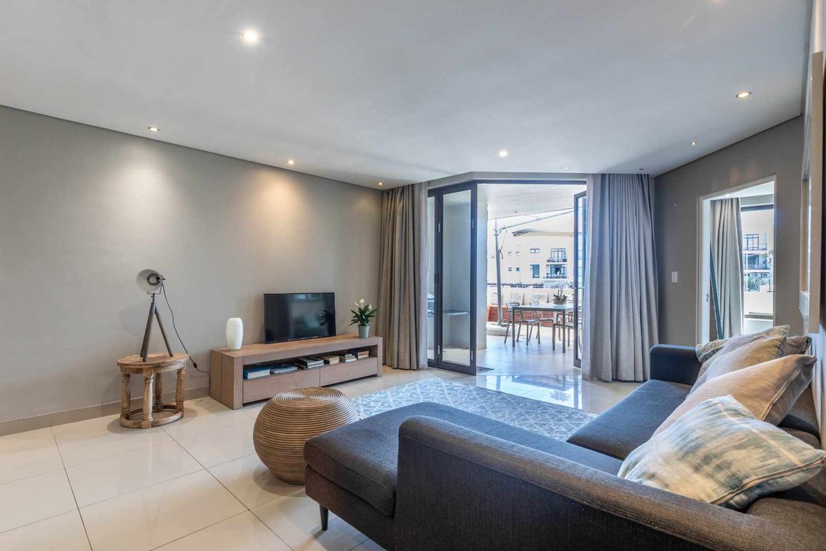Modern open-plan living area featuring tiled flooring, recessed downlighting, and seamless access to a private balcony through large glass sliding doors.