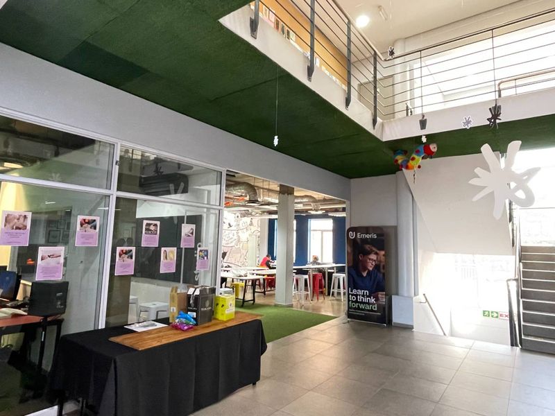 Modern open-plan office space featuring a mezzanine level, glass-partitioned rooms, tiled flooring, and an industrial-style exposed ceiling.