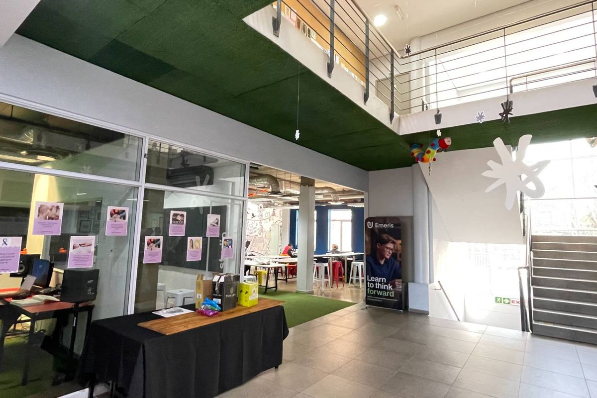 Modern open-plan office space featuring a mezzanine level, glass-partitioned rooms, tiled flooring, and an industrial-style exposed ceiling.