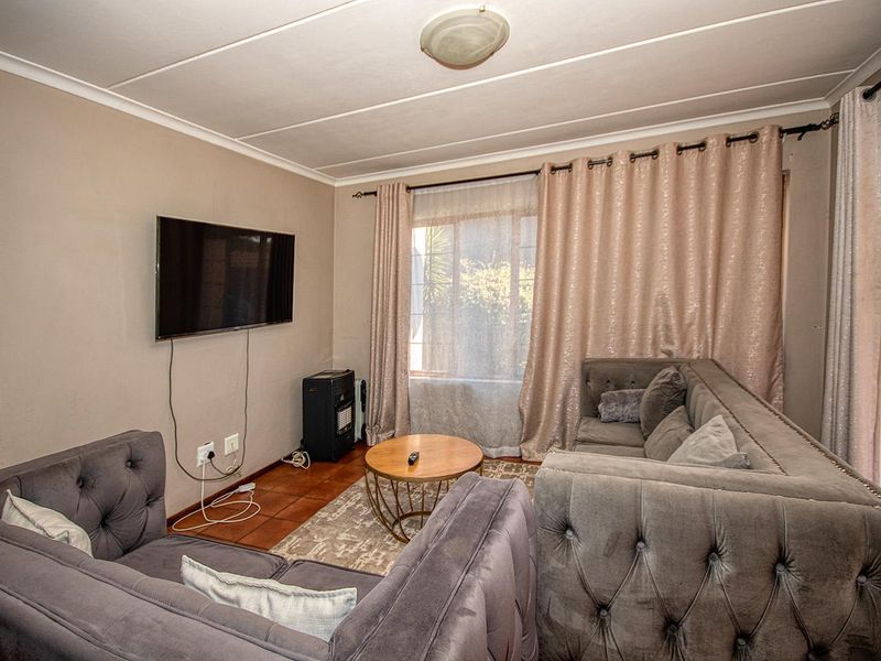 A comfortable living room featuring tiled flooring and large windows with curtain rods, providing a functional space for relaxation.