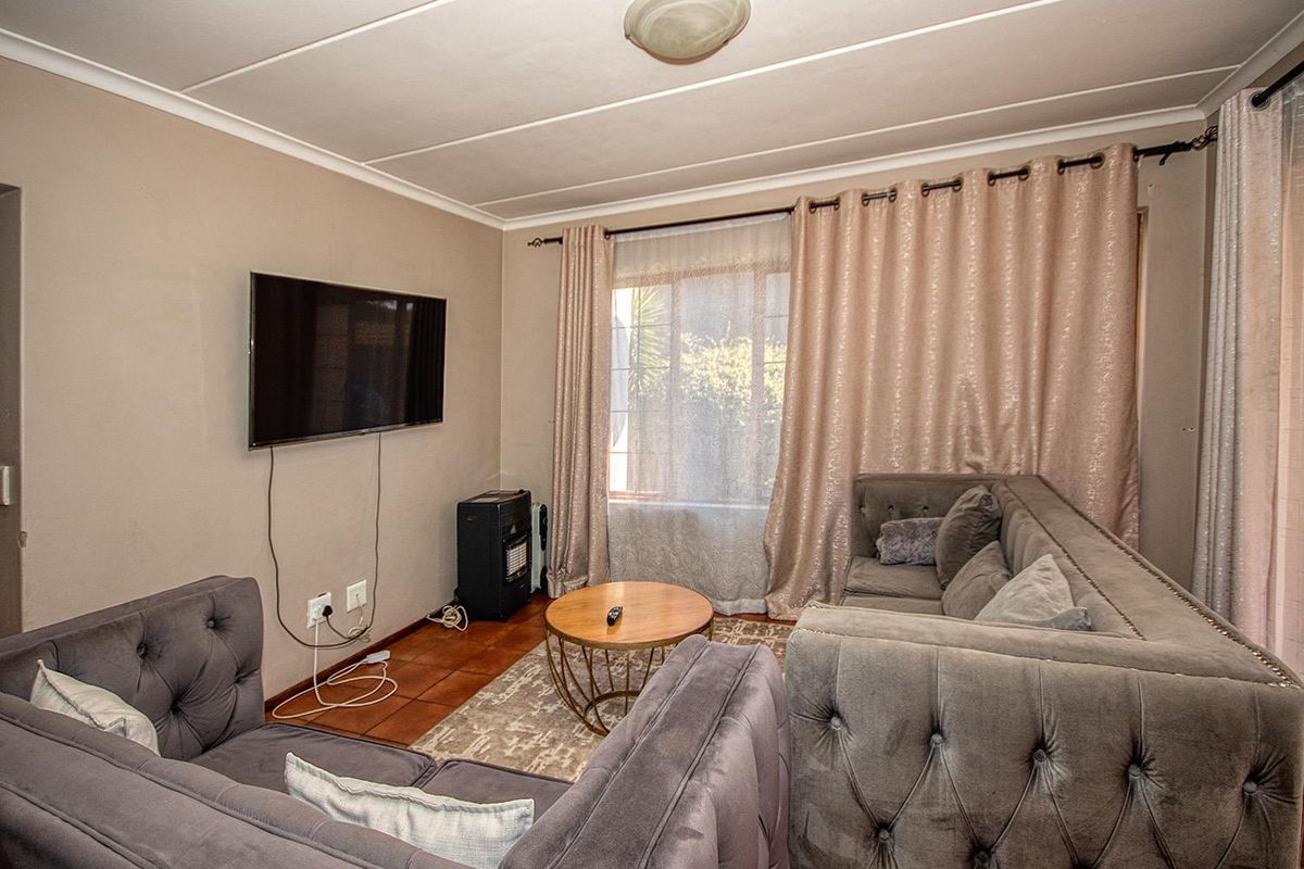 A comfortable living room featuring tiled flooring and large windows with curtain rods, providing a functional space for relaxation.
