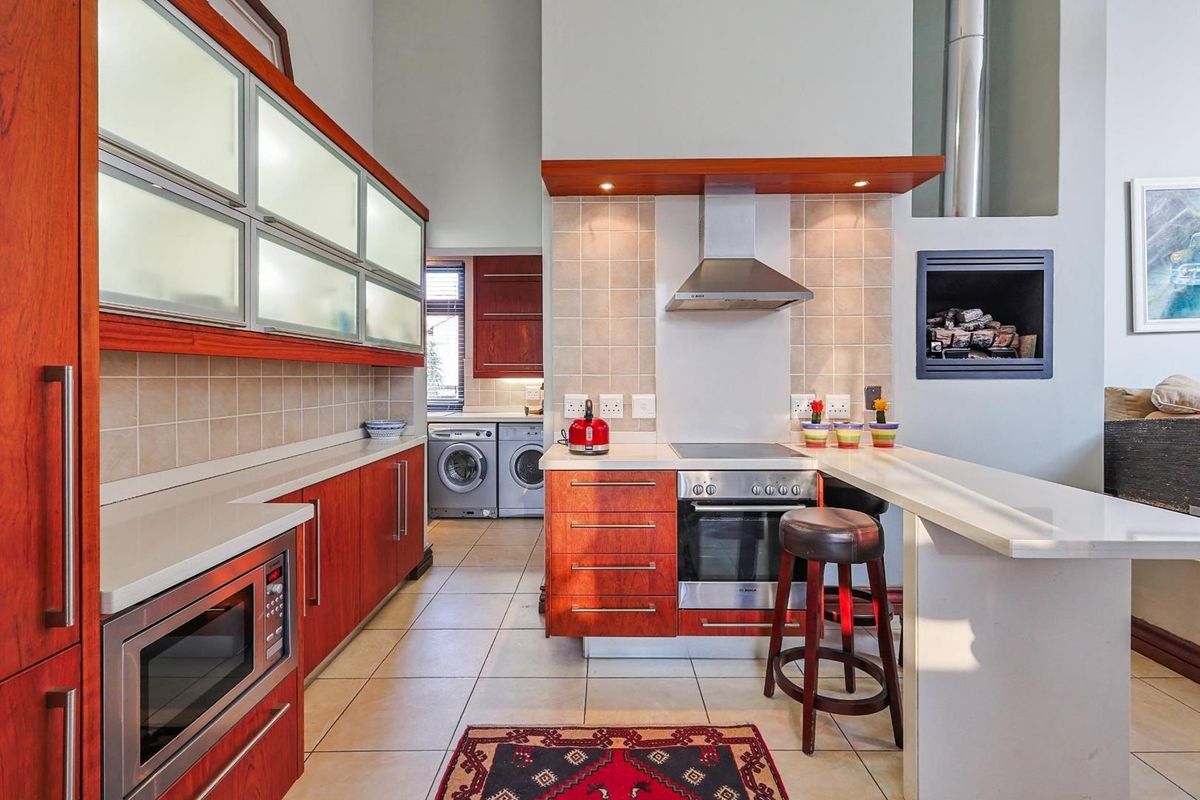 Modern kitchen featuring cherry wood cabinetry, stone countertops, built-in oven, extractor fan, and a breakfast bar, with an adjacent laundry area.