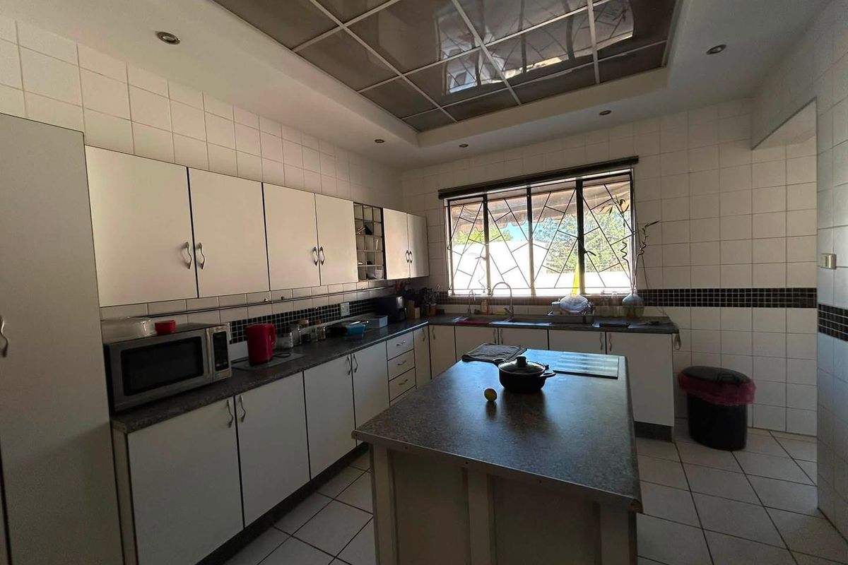 A functional kitchen featuring white cabinetry, a central island, tiled surfaces, and a large window with security bars, offering a practical workspace.