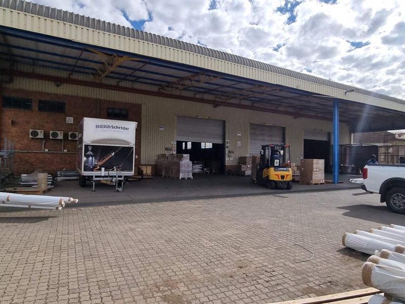 Industrial warehouse exterior featuring a large covered loading bay, multiple roller shutter doors, and paved yard area suitable for logistics and storage operations.