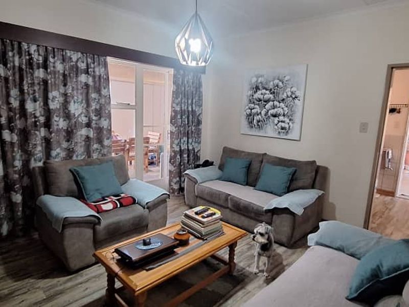A comfortable living room featuring laminate flooring, a central pendant light, and a sliding glass door providing access to the outdoor patio area.