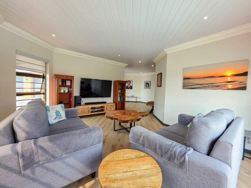 A bright and well-maintained living room featuring timber-look flooring, a tongue and groove ceiling with recessed lighting, and louver windows.