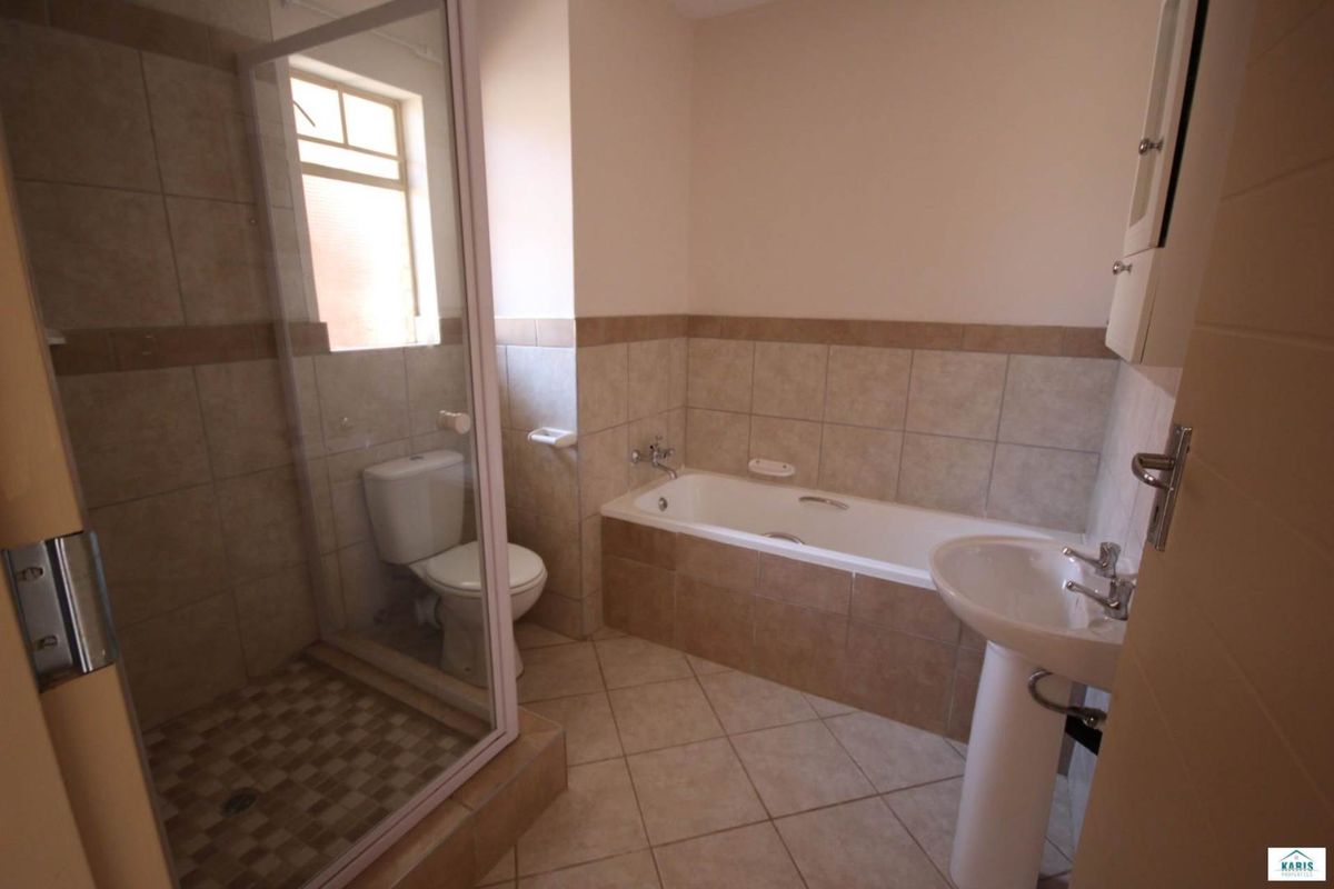 A functional bathroom featuring a separate shower enclosure, a built-in bathtub, a pedestal basin, and a toilet with neutral wall and floor tiling.