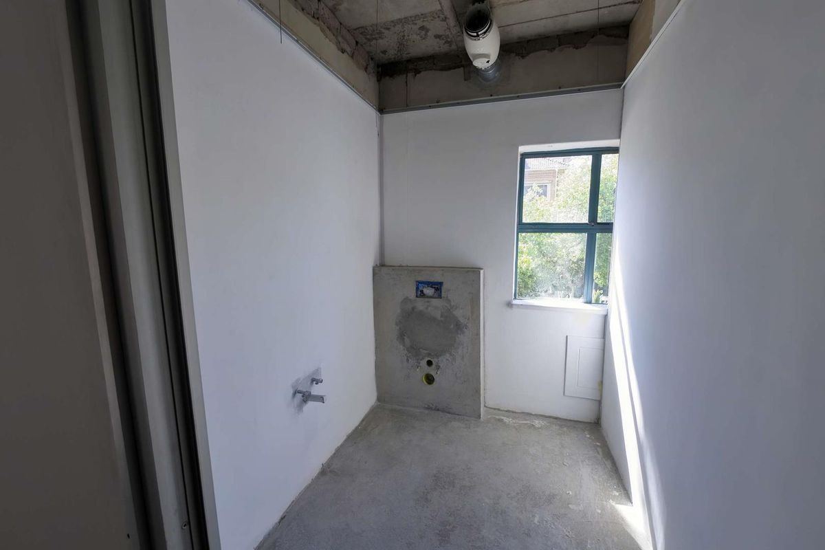 An unfinished office bathroom space featuring exposed concrete ceilings, rough plumbing connections, and a window, ready for final fit-out and finishes.
