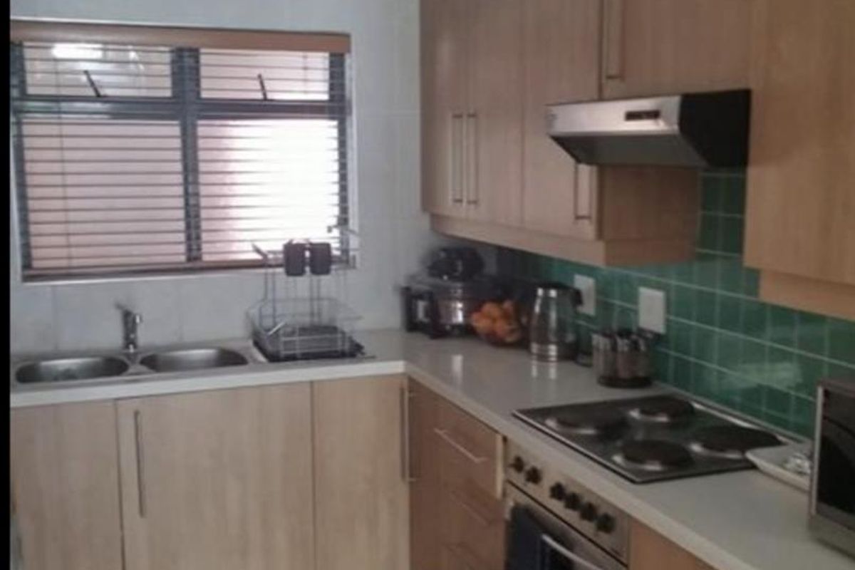 A functional kitchen featuring light wood cabinetry, stone countertops, a built-in oven with electric hob, and a green tiled splashback.