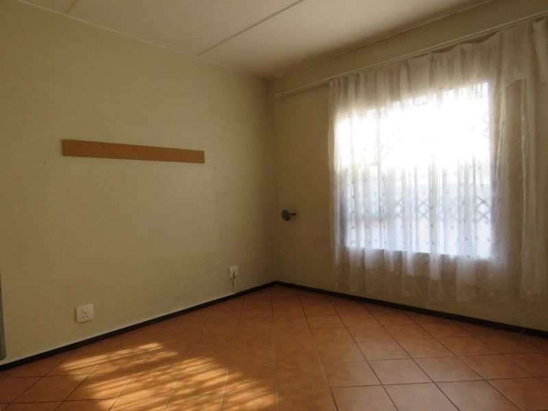 An empty bedroom featuring tiled flooring and a window with a security gate, requiring minor cosmetic updates to the wall finishes.