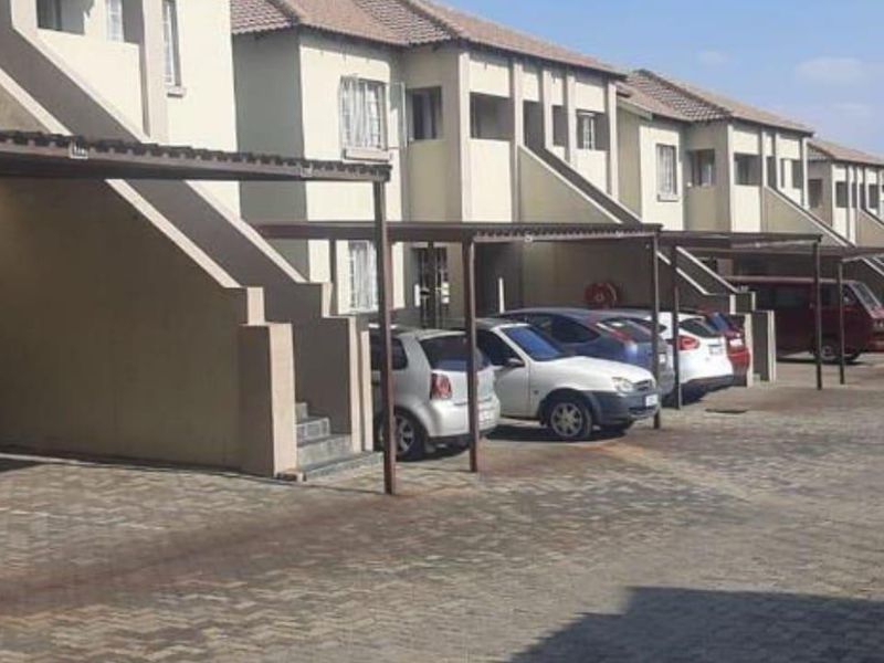 Exterior view of a townhouse complex featuring a row of covered carports and paved driveway access.