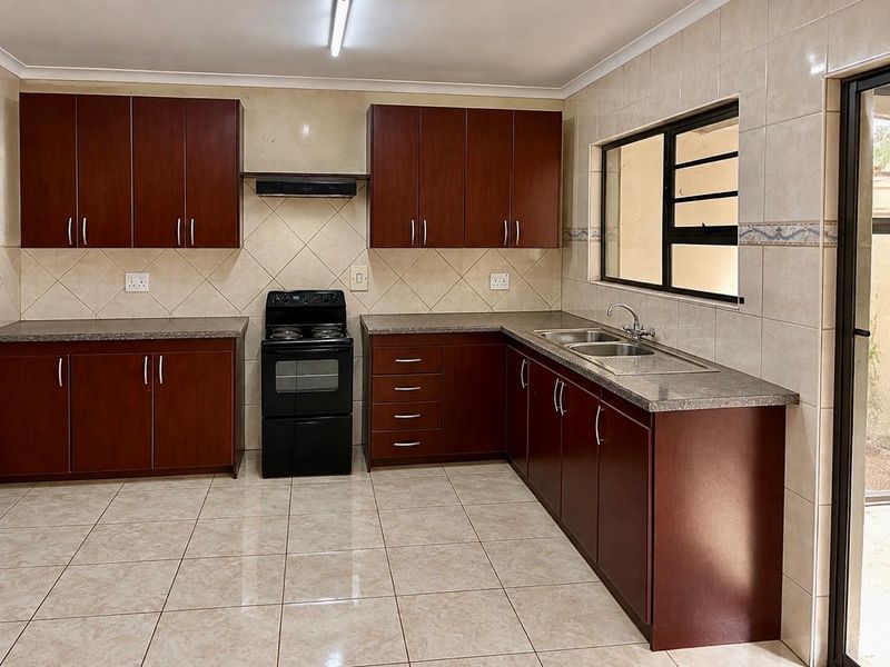 A functional kitchen featuring dark wood cabinetry, laminate countertops, a double sink, and a freestanding stove with an extractor fan.