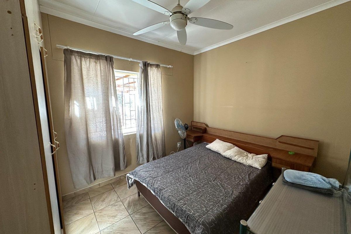 A functional bedroom featuring tiled flooring, a built-in wooden headboard with integrated side tables, and a ceiling fan.
