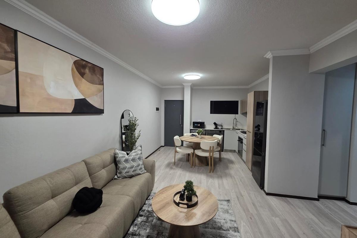 Modern open-plan living area featuring a compact kitchen with built-in cabinetry and light-toned laminate flooring throughout.