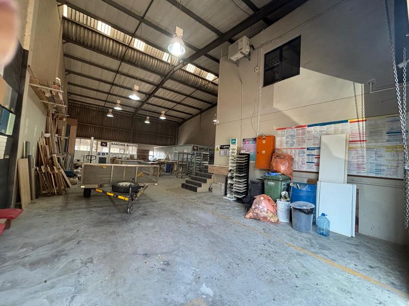 Spacious industrial workshop area featuring high-bay lighting, exposed steel roof structure, concrete flooring, and a mezzanine level suitable for various commercial or manufacturing operations.