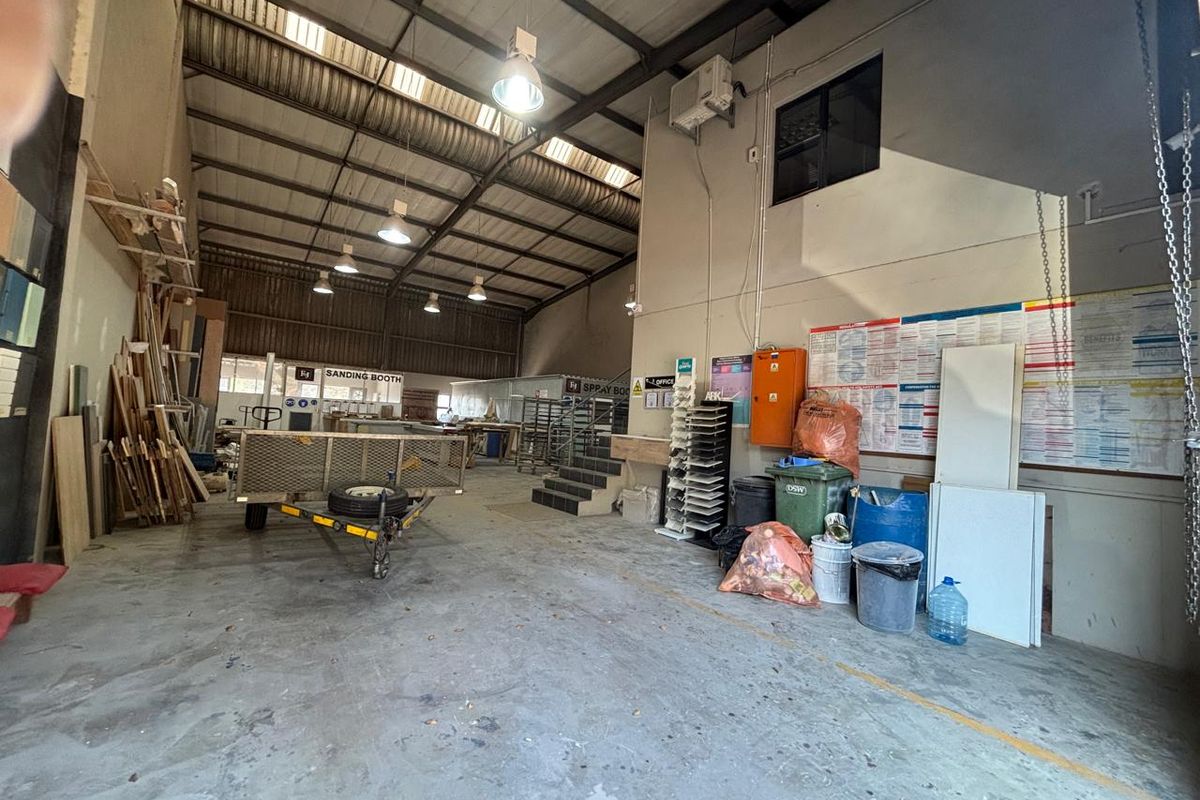 Spacious industrial workshop area featuring high-bay lighting, exposed steel roof structure, concrete flooring, and a mezzanine level suitable for various commercial or manufacturing operations.
