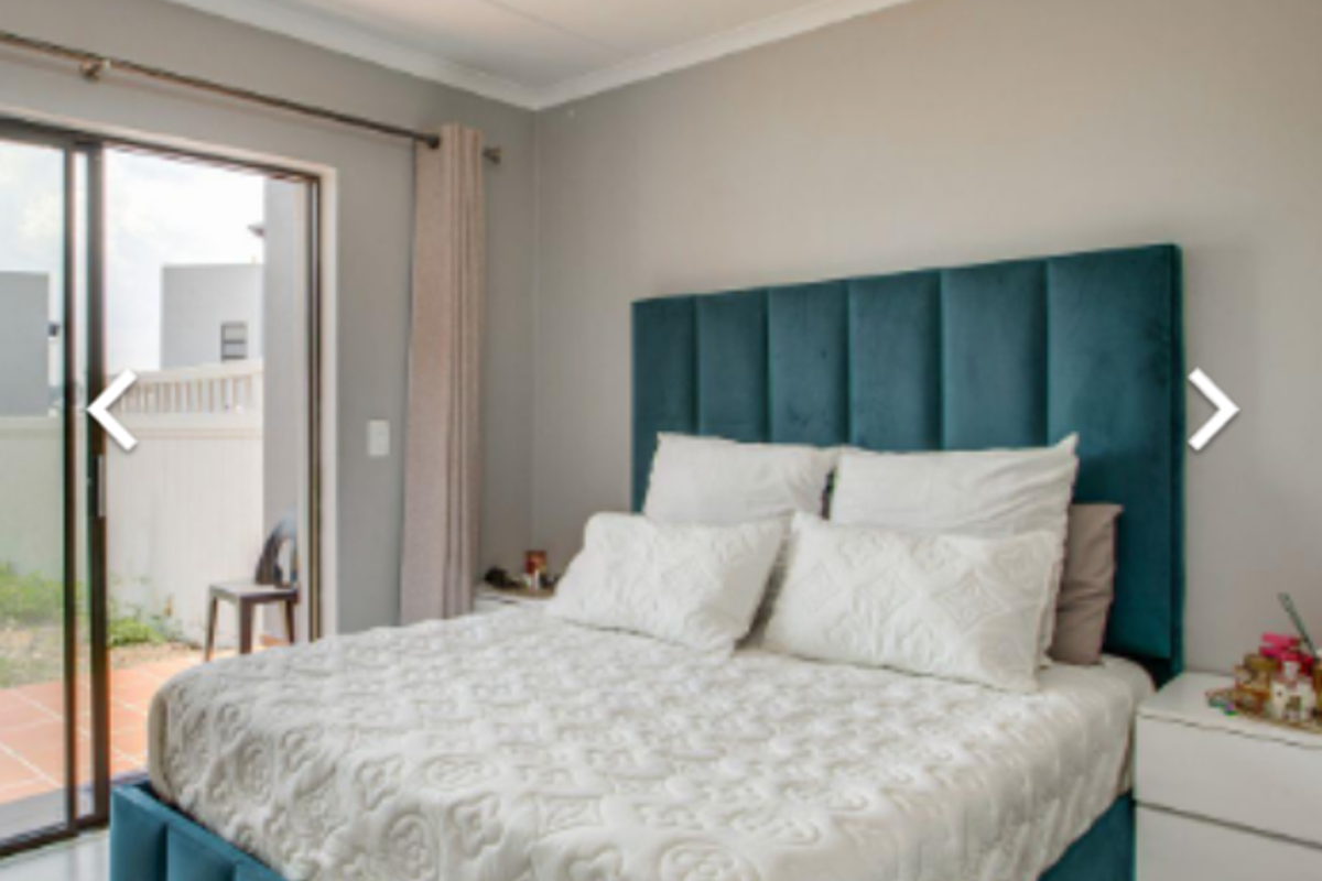 A well-lit bedroom featuring light wood-look flooring, neutral walls, and sliding glass doors providing direct access to an outdoor patio area.