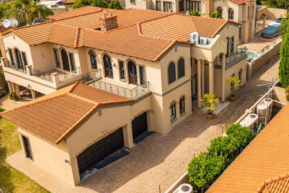 Aerial view of a large multi-story residential property featuring a terracotta tile roof, paved driveway, double garage, and multiple balconies.