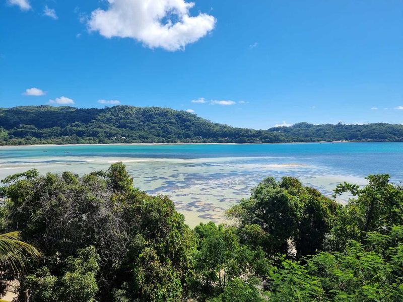 A scenic elevated view overlooking a tropical coastline with turquoise waters, coral reefs, and lush green hills under a clear blue sky.
