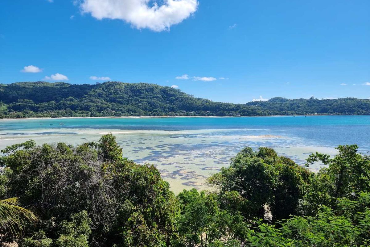A scenic elevated view overlooking a tropical coastline with turquoise waters, coral reefs, and lush green hills under a clear blue sky.