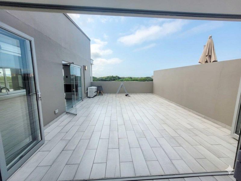 A spacious, open-air balcony featuring modern light-toned tiled flooring and glass sliding door access, offering an expansive outdoor area.