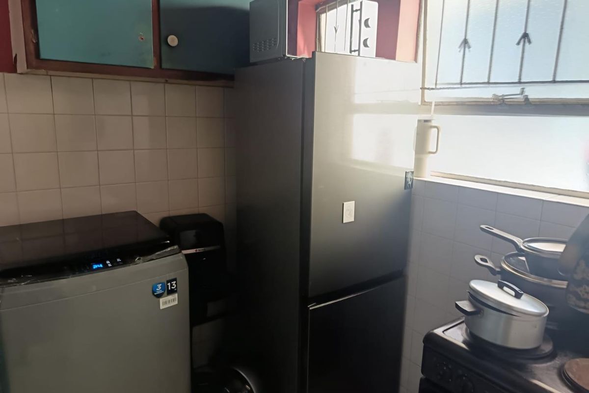 A compact kitchen area featuring tiled splashbacks, upper cabinetry, and a window with security bars.