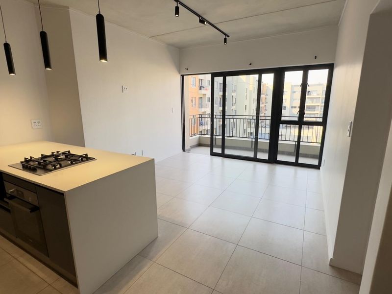 Modern open-plan living area featuring a sleek kitchen island with gas hob, tiled flooring, and large sliding doors opening to a private balcony.
