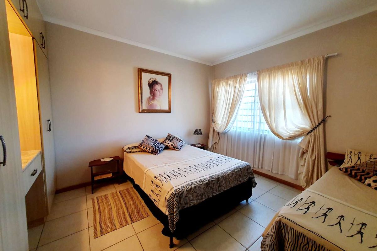 A bedroom featuring tiled flooring, built-in cabinetry with a vanity section, and large windows with curtains.