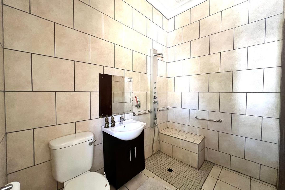 A functional bathroom featuring floor-to-ceiling wall tiles, a walk-in shower with a built-in tiled bench, a vanity basin, and a toilet.