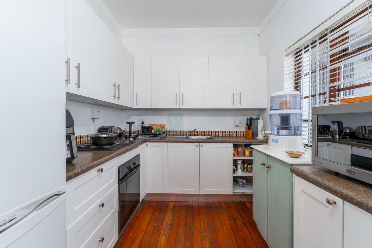 A functional kitchen featuring white cabinetry, dark laminate countertops, a built-in oven, gas hob, and original wooden flooring.